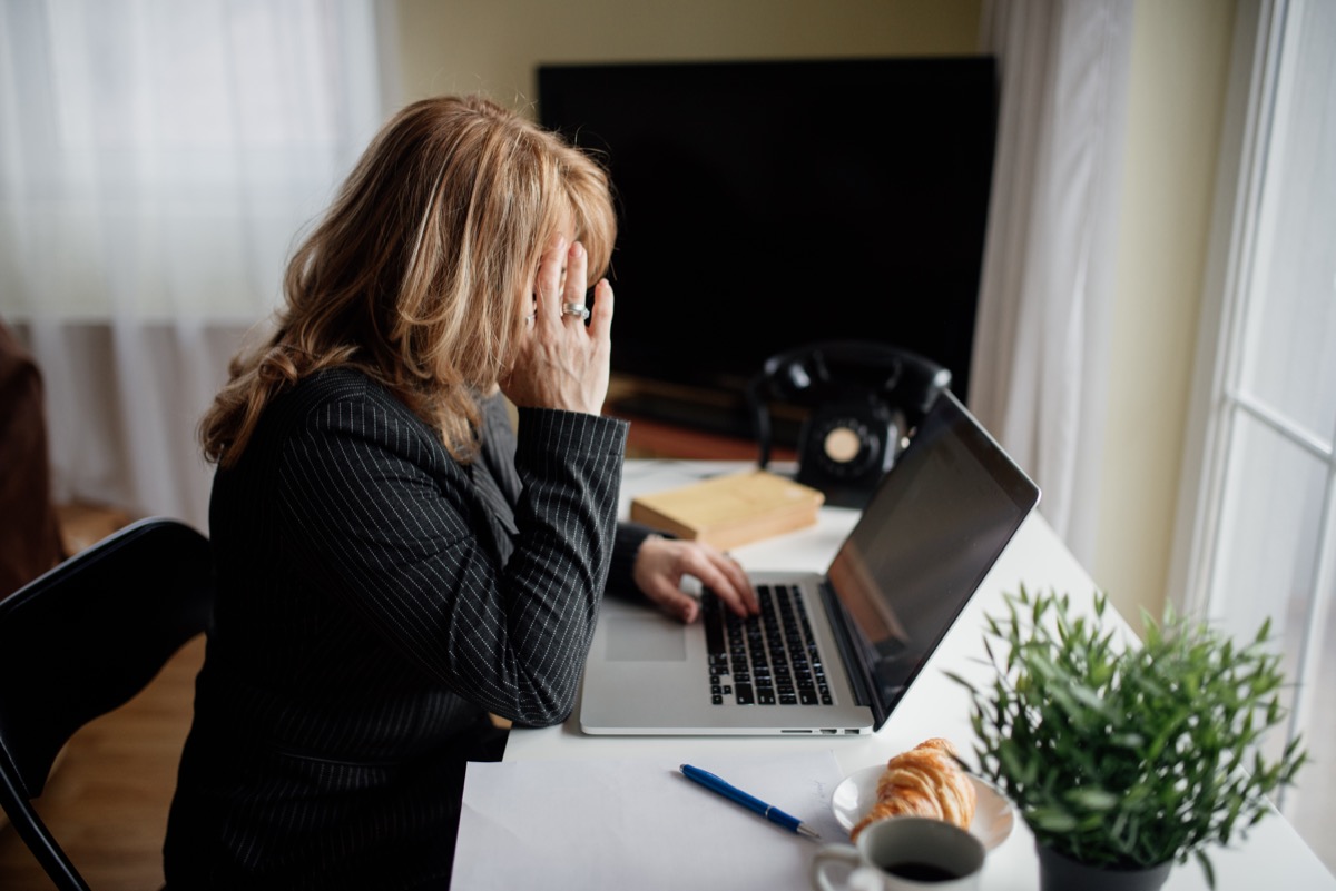 Një grua në tavolinën e saj duke mbuluar fytyrën me duart, dukshëm e mbingarkuar dhe e shteruar