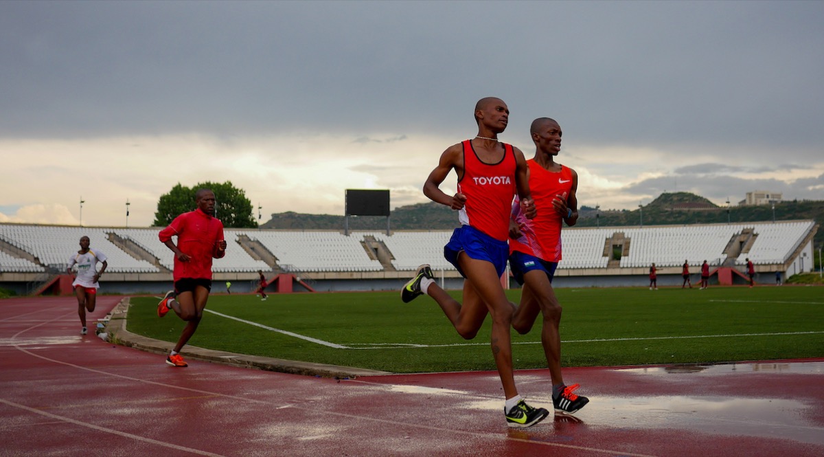 Athletes running neck and neck on a track in Maseru, Lesotho — consistent training over months separates those who improve from those who plateau