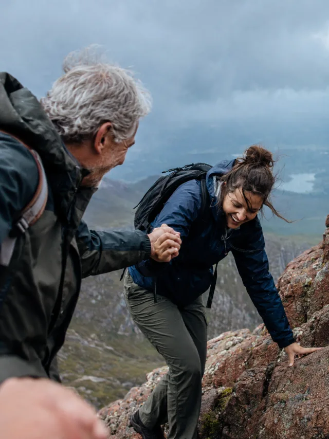 A hiker helping another hiker up a rocky mountain trail