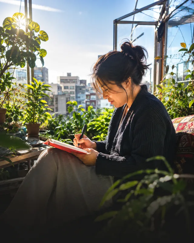 A woman reflecting in a journal on a sunlit terrace