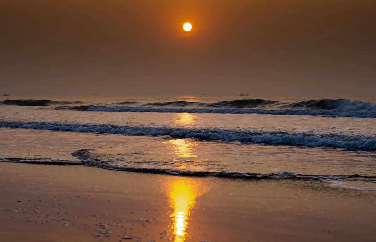 Waves rolling toward a beach beneath a low golden sun