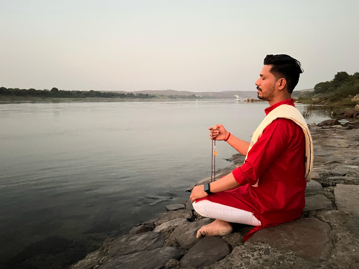 Person meditating by a river at dawn