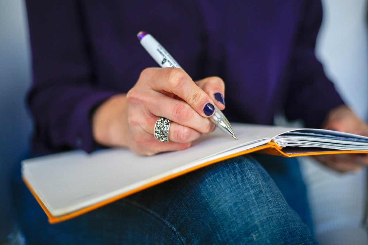 A woman writing in a notebook with a pen — tracking habits and commitments on paper